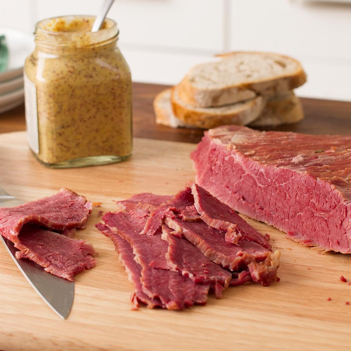 切菜板上的一片腌牛腩。背景是一罐芥末和黑麦面包。