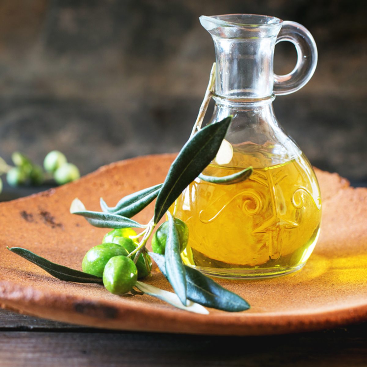 一瓶橄榄油和橄榄枝放在手工制作的陶土盘上，放在木桌上。