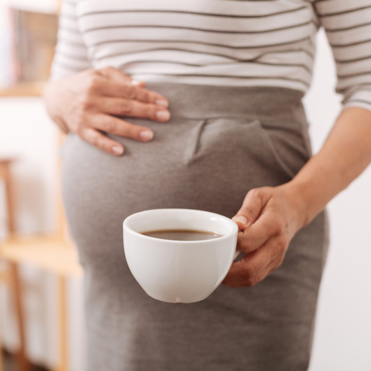 可爱的孕妇端着一杯咖啡