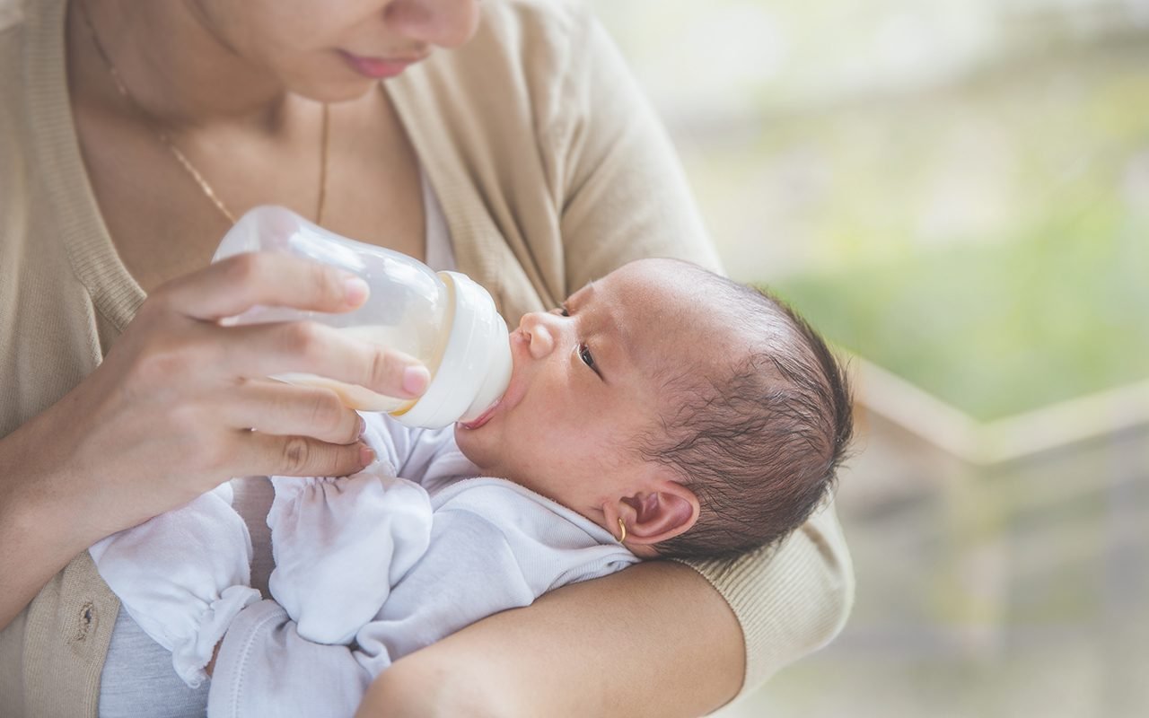 一幅可爱的新生儿肖像，她的妈妈正在用奶瓶喂她