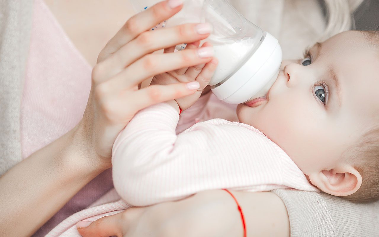 年轻的妈妈正在给她可爱的小女儿喂婴儿配方奶粉。