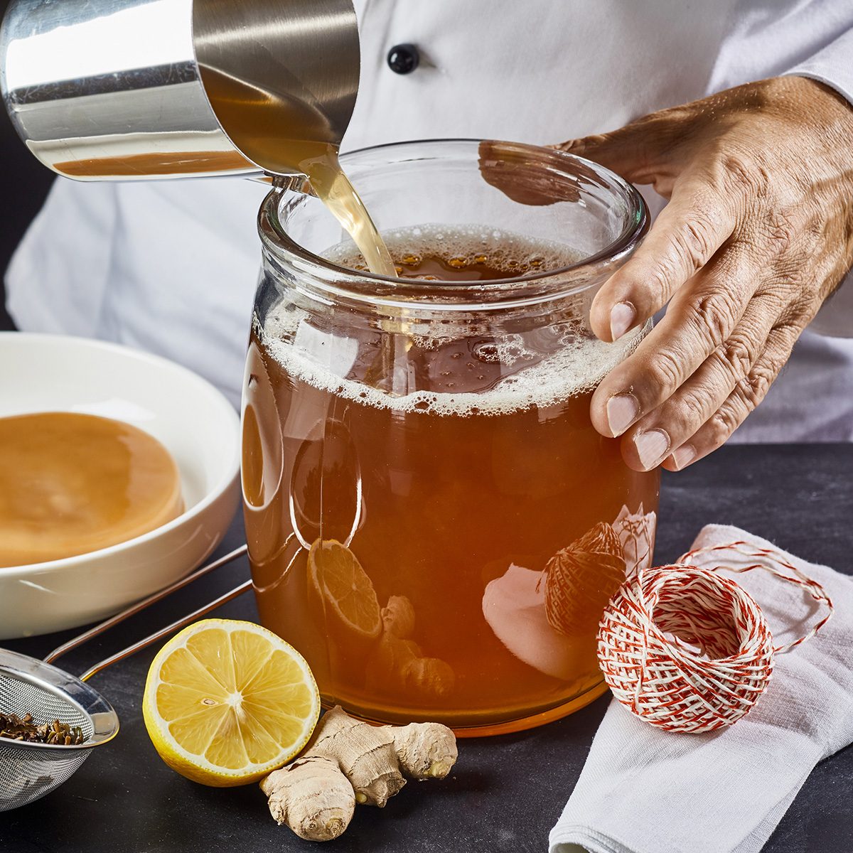 一名男子在自制康普茶的同时，将加了糖的红茶倒入灭菌玻璃罐中，准备加入scoby