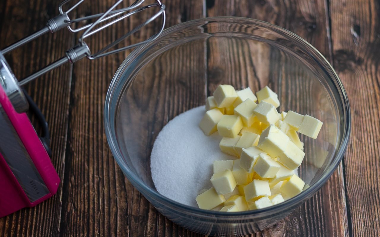 如何把黄油和糖搅成奶油。一碗黄油和糖，放在手动搅拌机旁边。