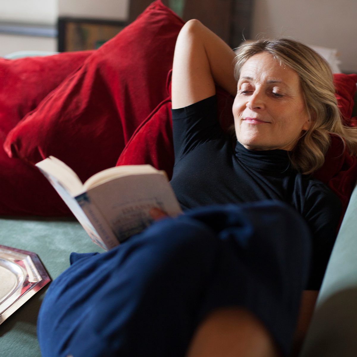 美丽成熟的女人放松在沙发上的一杯茶和一本书