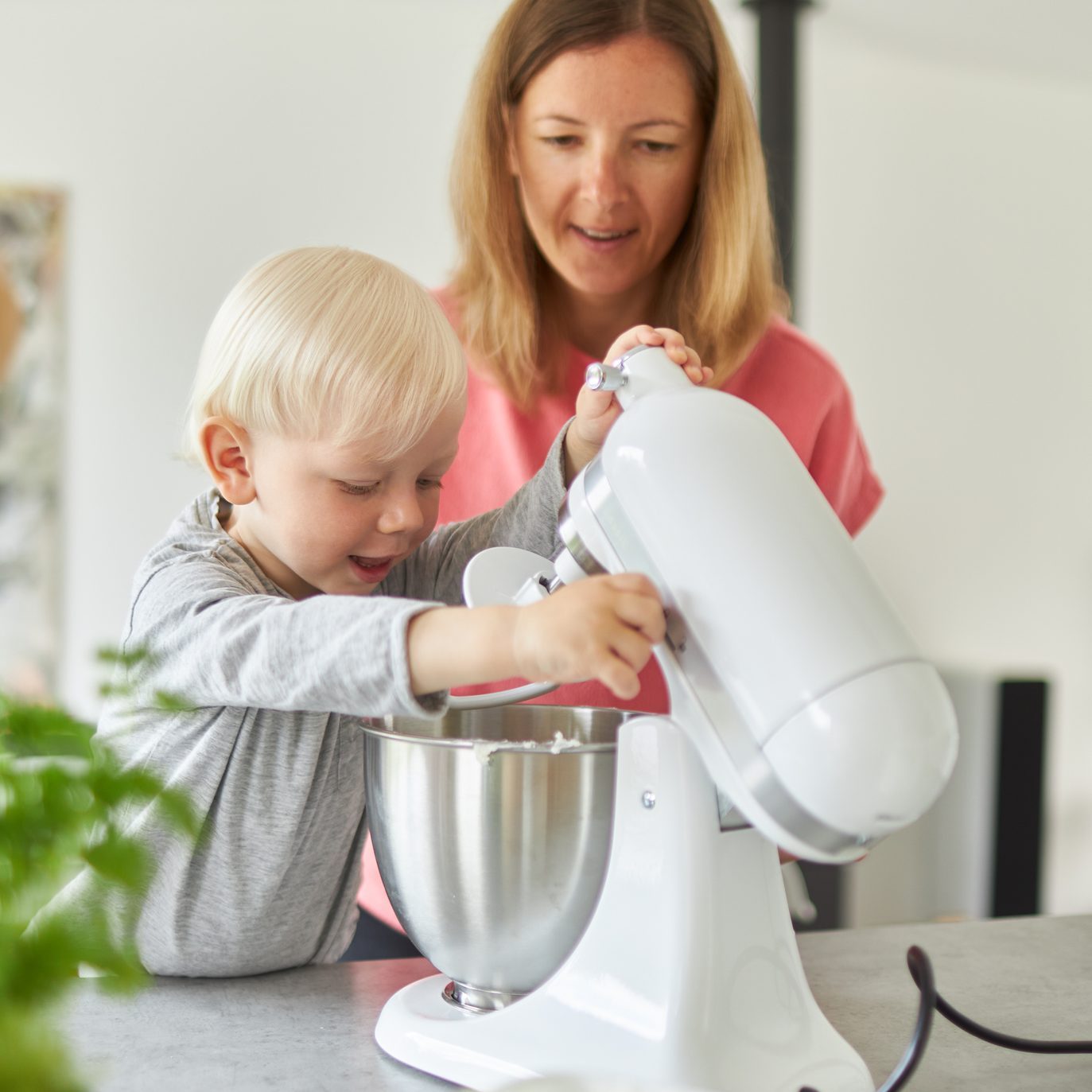 一位母亲带着她的金发儿子在她现代化的厨房里烤面包，教他如何操作食品加工机，并在面团做好后正确洗手。