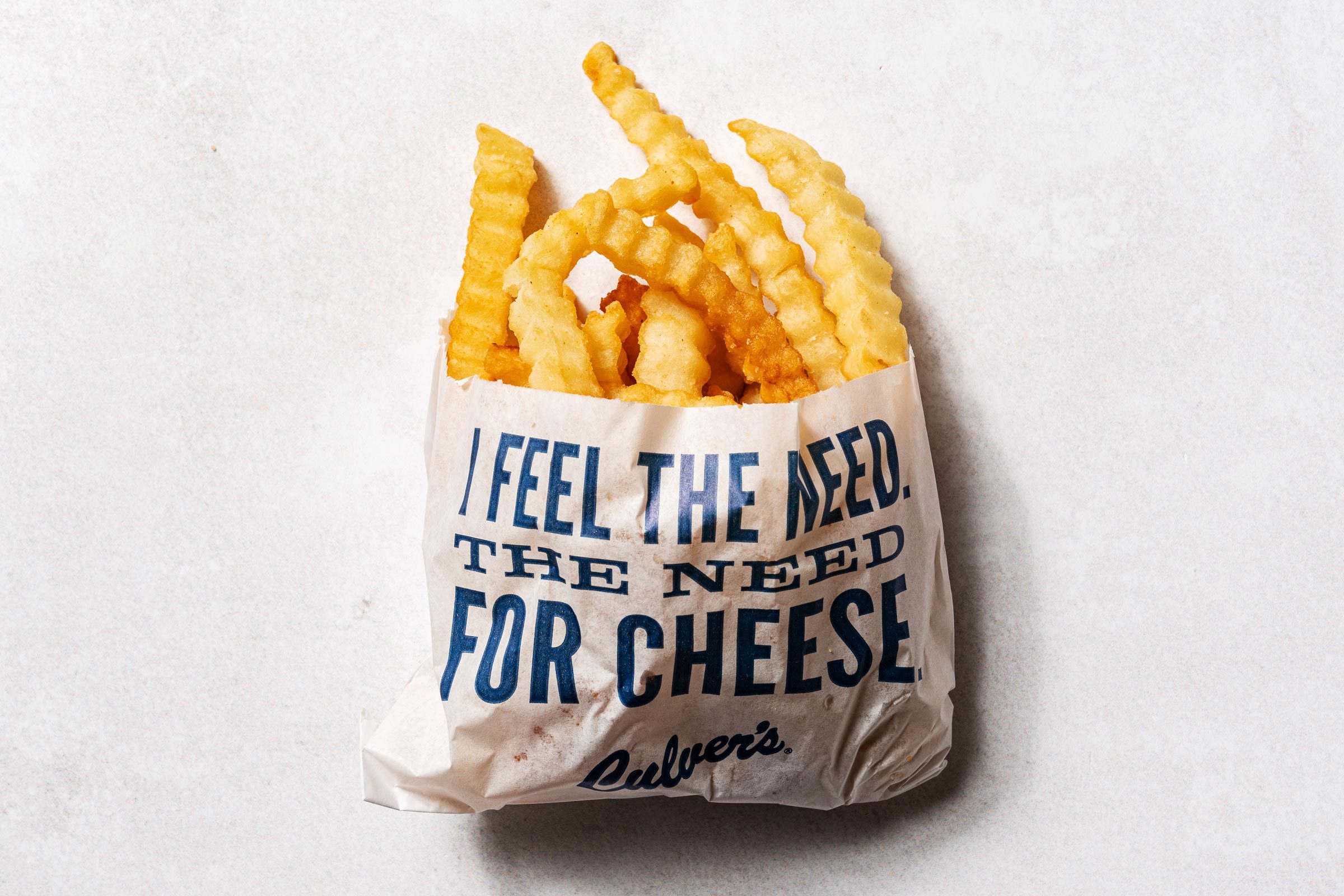 culvers在一个蜡袋中调薯条，上面写着“感觉需要奶酪”的蓝色字母