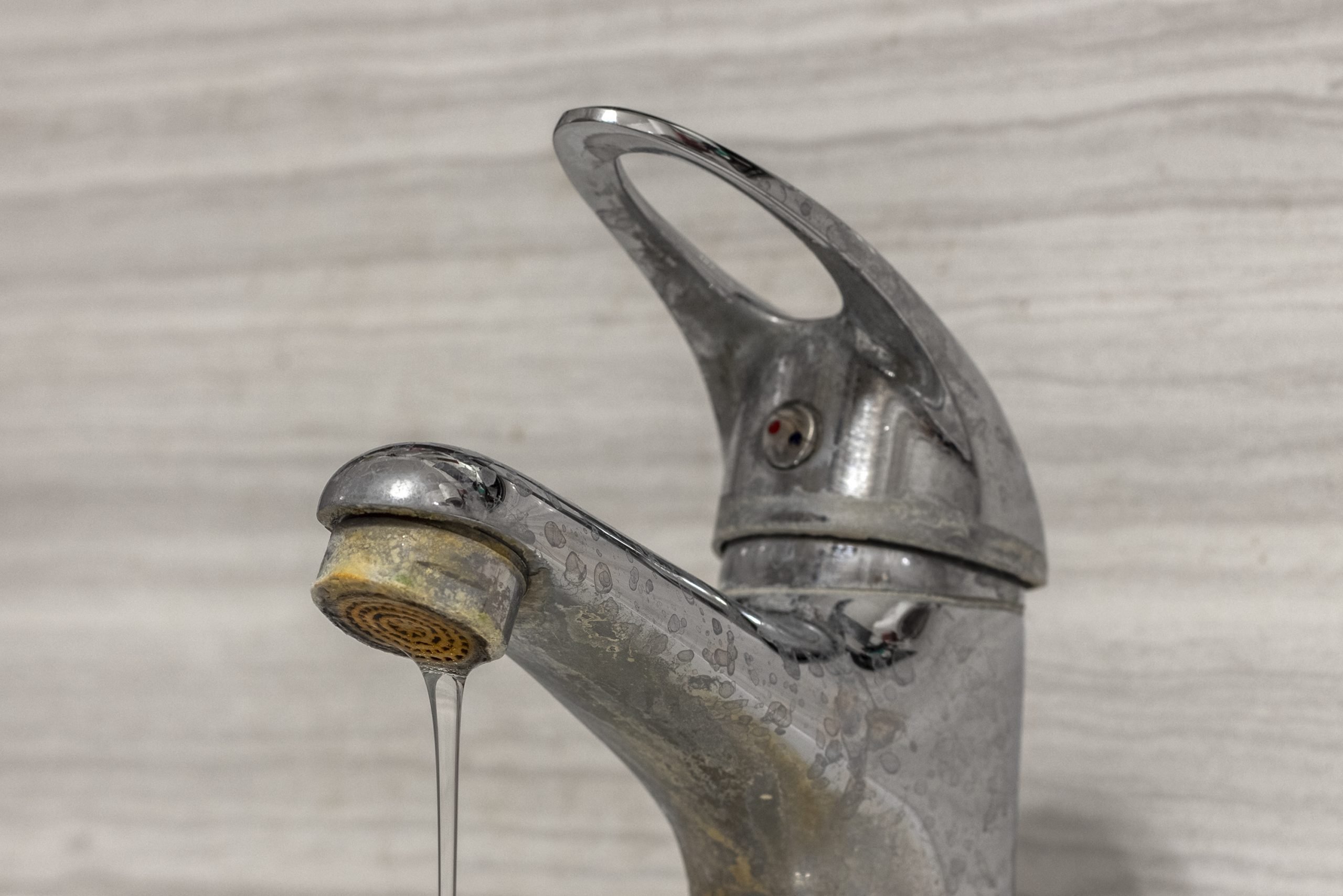 一股细细的硬水从一个旧的自来水曝气器中流出。旧浴室水槽水龙头被钙和污垢污染。