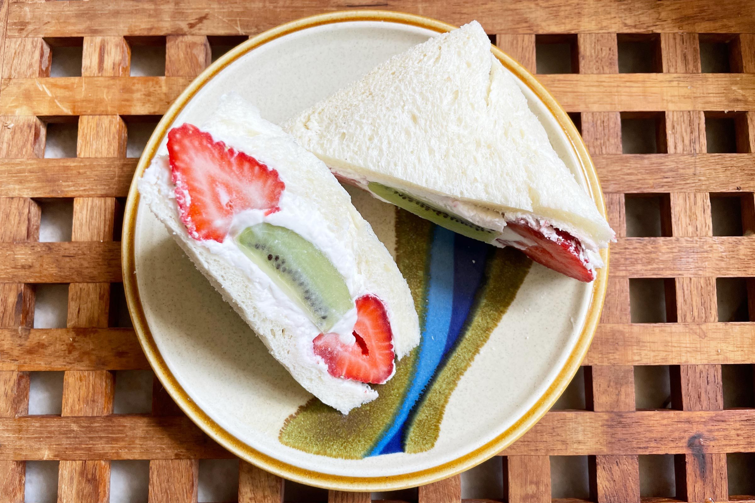 日式水果三明治，猕猴桃和草莓切成三角形放在盘子里，背景是木制的