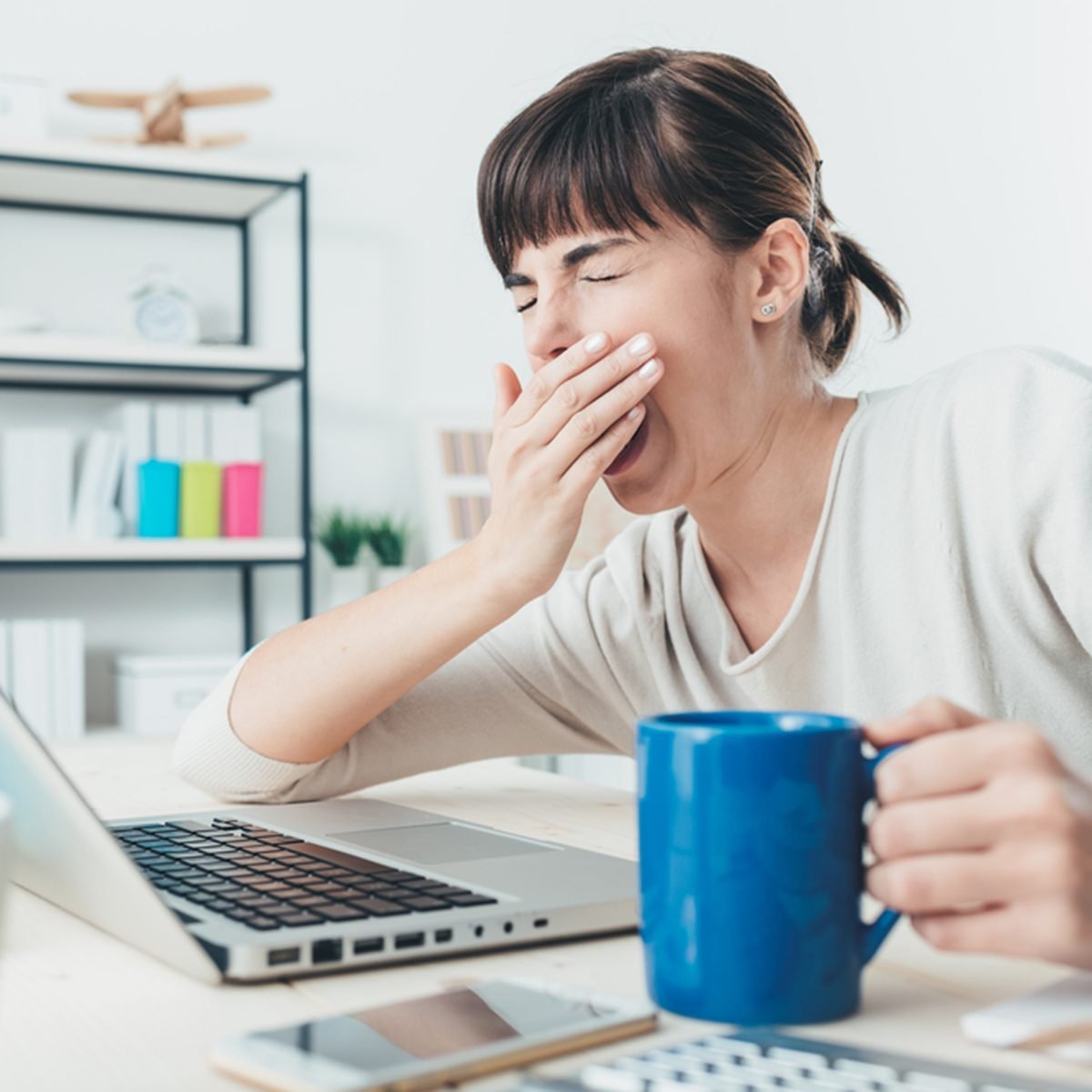 疲倦困倦的女人打着哈欠，在办公桌前工作捧着一杯咖啡，过度劳累和睡眠剥夺概念;Shutterstock ID 367741853