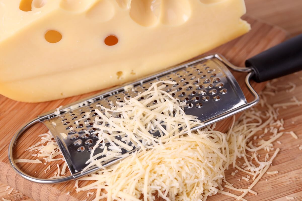 磨碎的奶酪和磨碎器放在木砧板上。