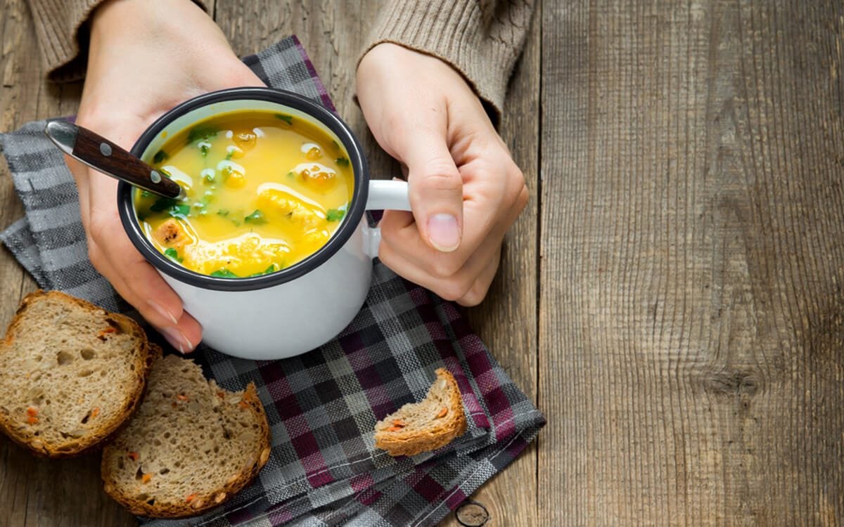 女人手拿着一碗蔬菜汤，配上欧芹和油炸面包丁——健康的冬季素食