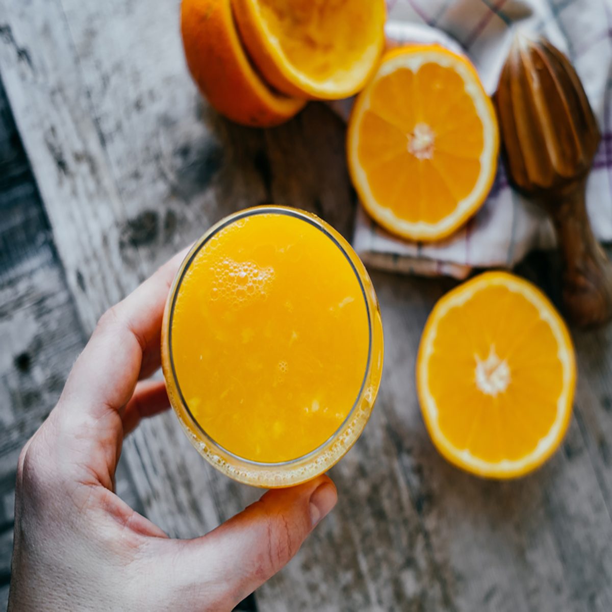 女人的手与果汁玻璃和橘子在木制背景。