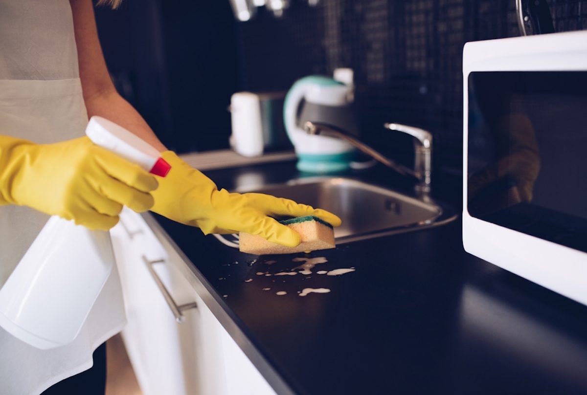 戴着黄色橡胶手套的女人用海绵清洁厨房橱柜的特写镜头
