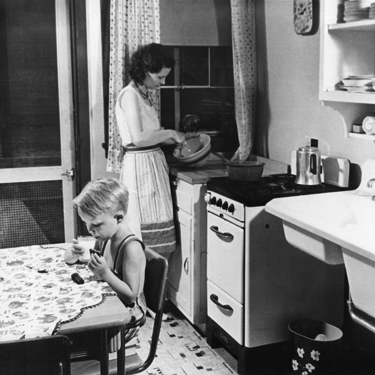 女人在厨房做饭，小男孩吃饼干加牛奶