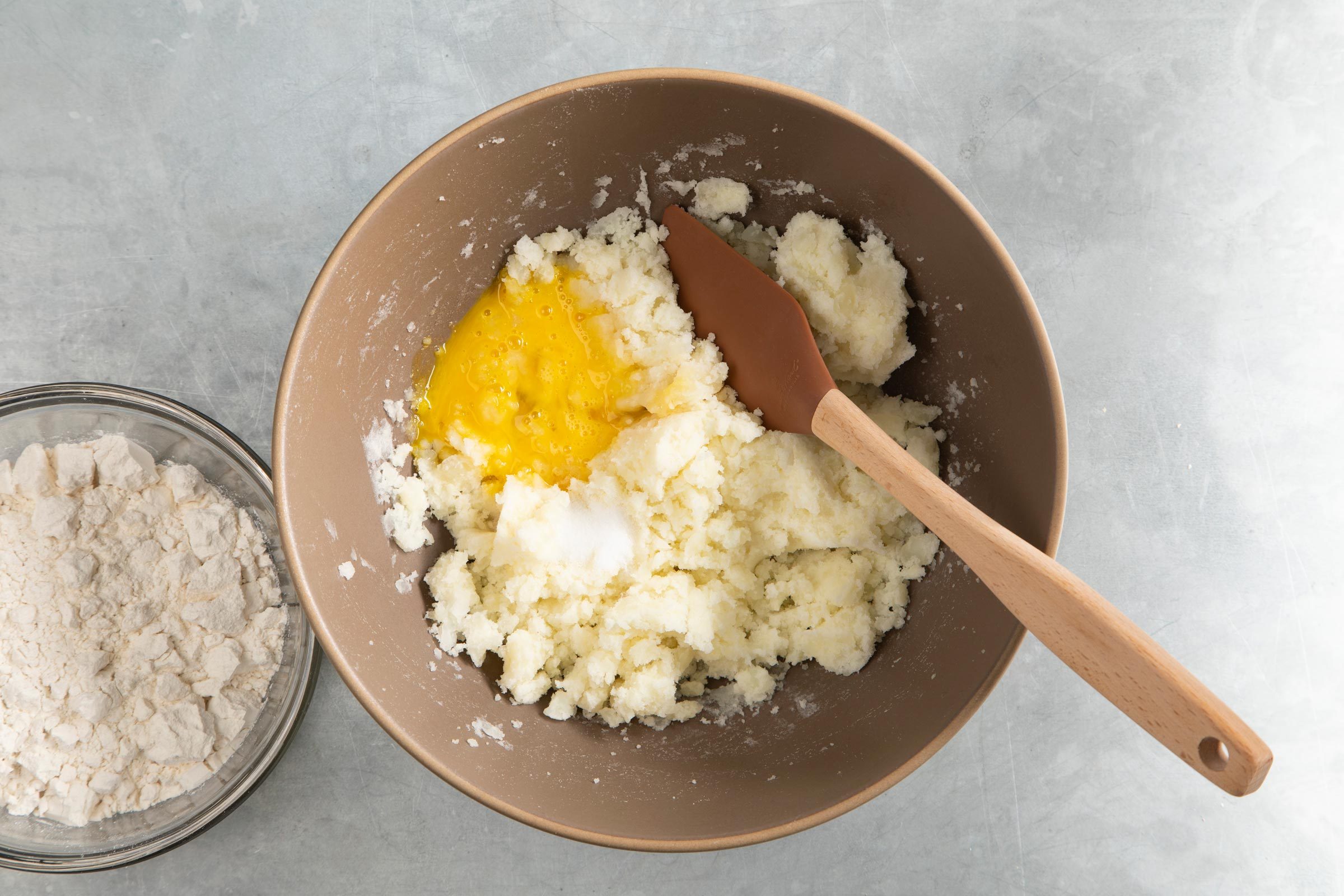 把土豆泥放在大碗里，加一个生鸡蛋和盐，准备混合。旁边放着一碗面粉。